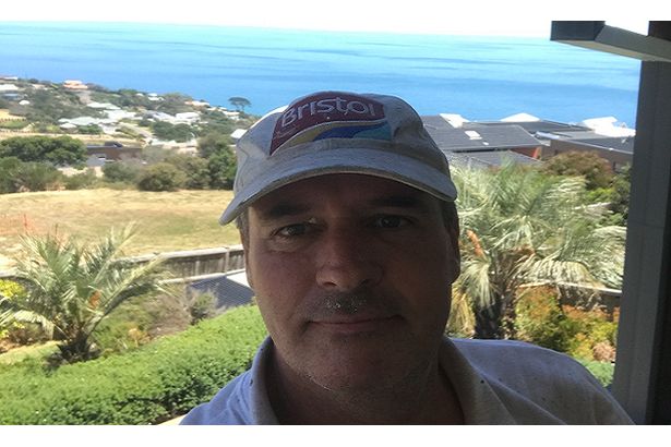 A man with a picturesque background of trees and houses.